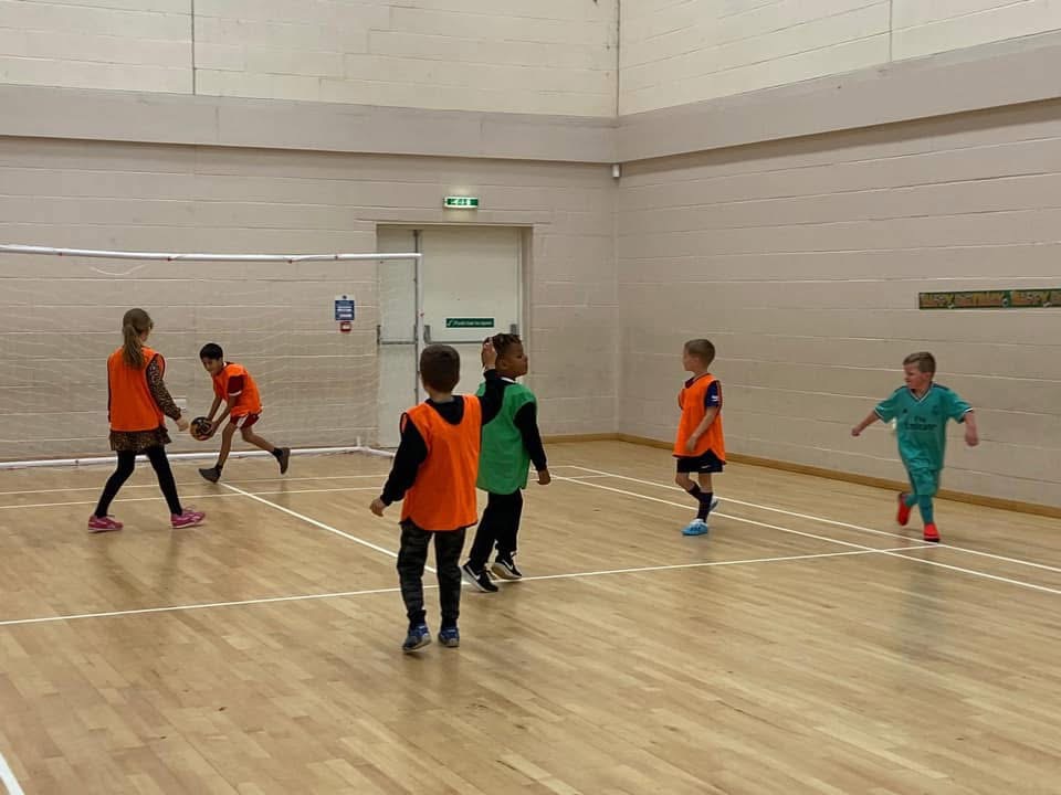 Children playing football indoors in bibs