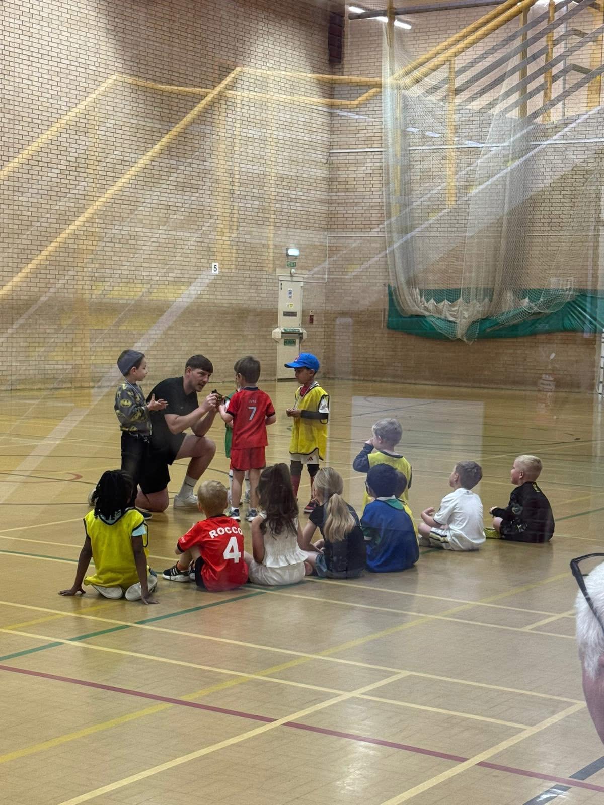 Qualified teacher coaching a group of children in a sports hall